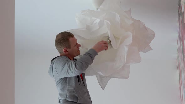 Repair and Home Decoration. a Man Hangs a Lamp in the Room From the Ceiling.