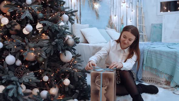 Caucasian Woman in Cozy Outfit Wraps a Gift Box in Christmas Decorated House