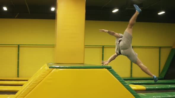 Male Gymnast Trains on Professional Trampoline Springs Over the Barrier with the Body Twist and