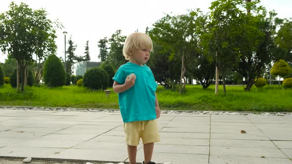 a Child in Bright Clothes Holds a Large Stone and Throws It Forward