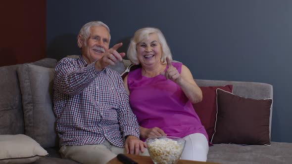 Senior Old Couple Holding Remote Control Talking Laughing Watching Humor Tv Show Sitting on Sofa