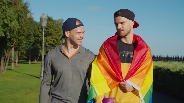 Two Male Lovers with Pride Flag Strolling in Park