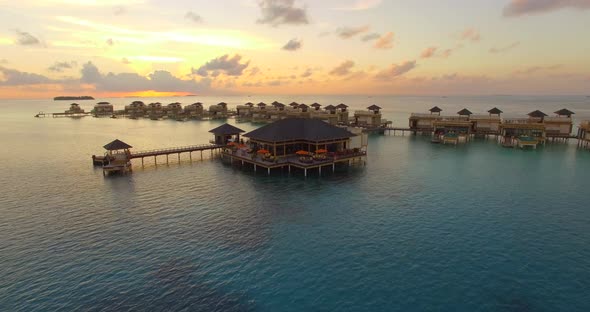 Aerial drone view sunset scenic tropical island, resort hotel with overwater bungalows, Maldives.