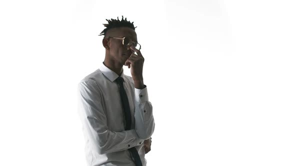 African-American man in office clothes and glasses stands on white background and thinks, touching