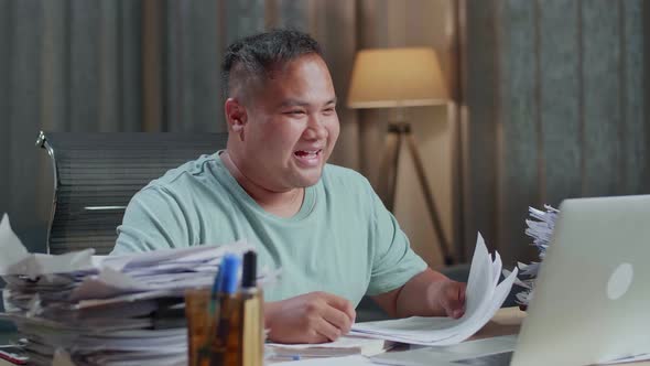 Close Up Of Fat Asian Man Having Video Call On Laptop While Working With Documents At The Office