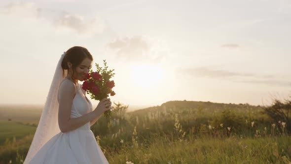 Smiling Young Bride Holds Flowers and Smells Them