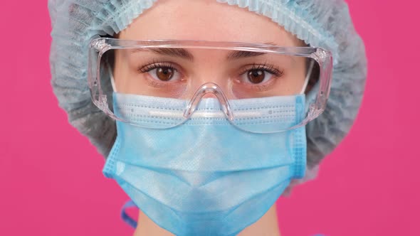 Close Up of Doctor in a Blue Medical Coat Safety Glasses and Medical Cap Looking at Camera