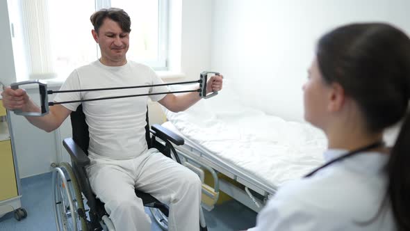 Weak Motivated Caucasian Man Exercising with Resistance Band Sitting in Wheelchair with Blurred