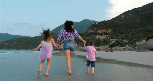 Young Family, Mother and Children Are Walking Along the Coast. Happy Family Walking on Sea Coast.