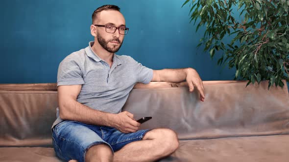 Pensive Male in Glasses Chatting Use Smartphone Sitting on Couch