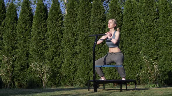 girl does Jumping fitness on trampoline in outdoor on green grass and trees on background