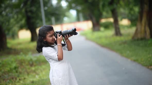 A cute little Asian girl is taking photos of nature and trees in a jungle with a Digital SLR camera