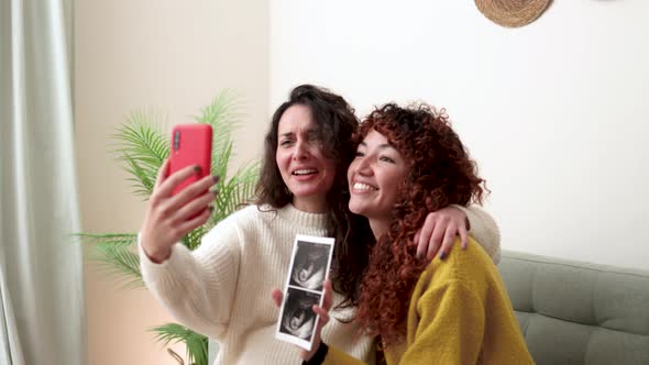 LGBT lesbian couple holding ultrasound photo scan on video call of growing baby in pregnancy time