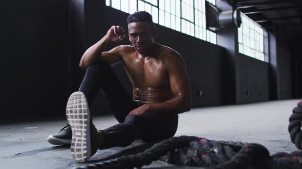 Shirtless african american man resting after battling ropes in an empty urban building