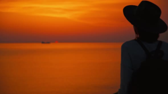 Young woman in a hat on vacation against the backdrop of the sunset sea