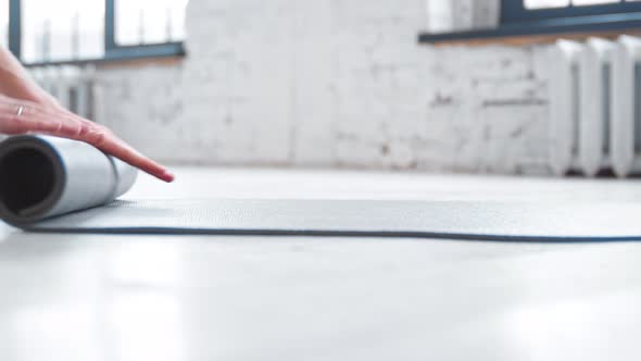 Female trainer hands roll grey rubber mat after training on parquet floor