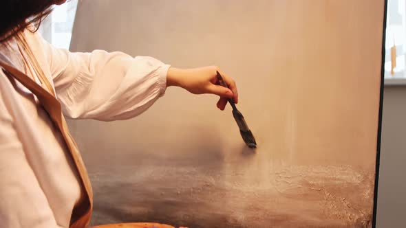 Art Studio  Young Woman Applying Painting Varnish on the Canvas with Finished Painting