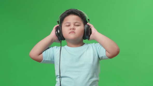 Asian Little Boy Listening To Music With Headphones And Dancing In The Green Screen Studio