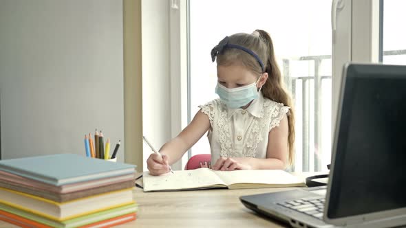 Little Schoolgirl in a Medical Mask Is Doing Her Homework. Learningduring the COVID-19 Epidemic.