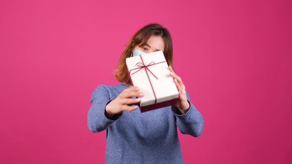 Young Woman That Wear a Medical Mask Offers a Gift Box While Looking in Camera