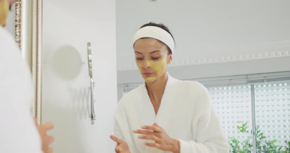 Caucasian woman looking in mirror and doing make up in bathroom