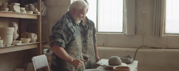 Senior Potter Teaching Young Woman to Throw on Wheel