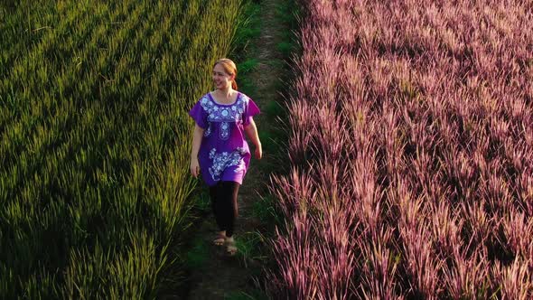 Asian Woman Walking At Green And Pink Rice Berry Field.