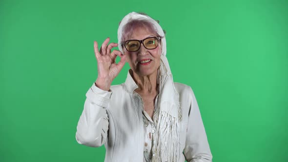 Portrait of Old Stylish Woman Is Making Sign Ok Isolated Over Green Background