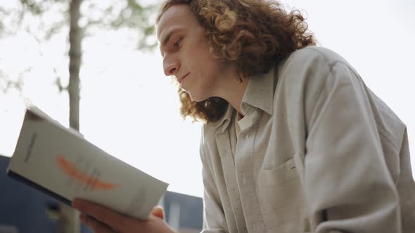 Pensive curly-haired man reading book