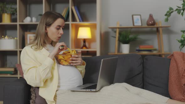 Expectant Mother Watching Film and Eating Snacks at Home