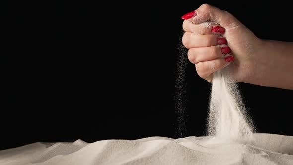 Female Hand Squeezing and Spilling Handful of White Dry Sand on Isolated Black Studio Background