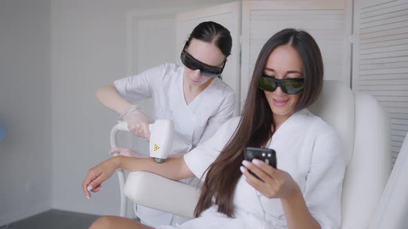 During a Laser Hair Removal Session a Woman in a Beauty Salon Writes a Message in Her Mobile Phone