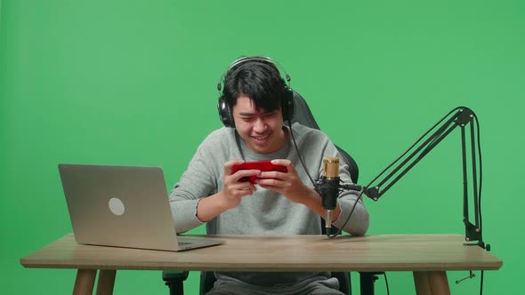 Asian Man Gamer With Headphone Using Mobile Phone Playing Game On The Green Screen