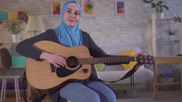 Young Muslim Musician Woman Tunes Her Guitar and Looks at the Camera