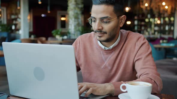 Slow Motion Portrait of Young Arab Guy Using Laptop and Drinking Coffee in Nice Cafe