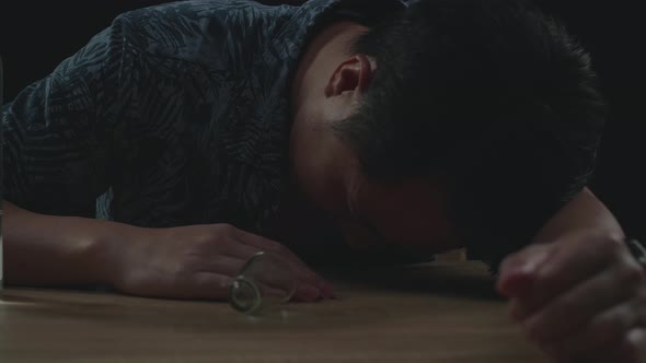 Drunk Asian Man Pouring Vodka In A Shot Glass Before Drinking And Sleeping In Black Background