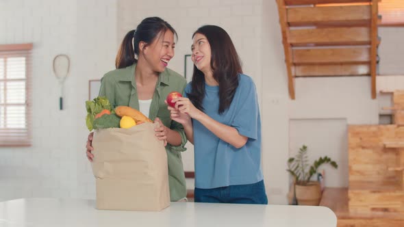 Asian Lesbian lgbtq women couple hold grocery shopping paper bags at home.