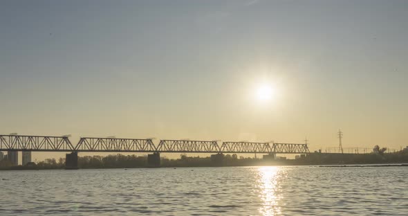 Timelapse of City River Bank. Sun Rays, Blue Sky and Railway Bridge Over Horizont. Summer Sunset