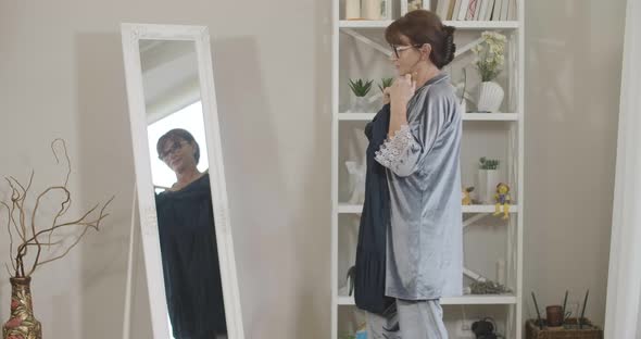 Side View of Stylish Senior Woman Looking in Mirror Trying on Blue Dress in the Morning
