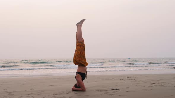 Serenity and Yoga practicingIs on the Head Woman Near Ocean Doing Headstand Upside Down