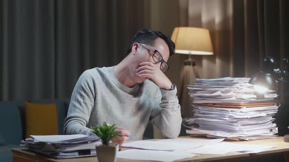 Tired Asian Man Yawning While Working Hard With Documents At Home
