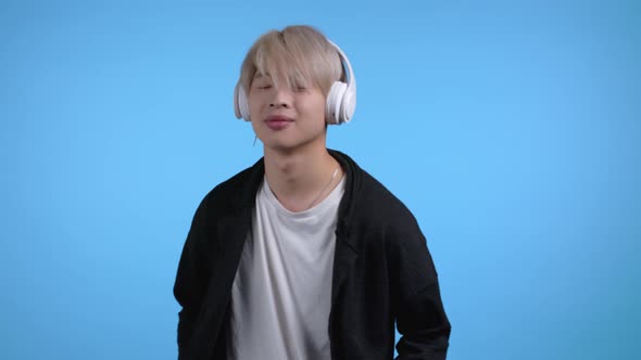 Handsome Korean Man with Trendy Blond Hairdo Having Fun Smiling with Headphones in Studio Against