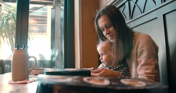 Young woman with baby girl in restaurant watching menu choosing food