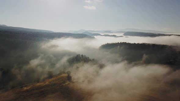 Aerial view of vast land in golden color enveloped in fog, zooming out shot