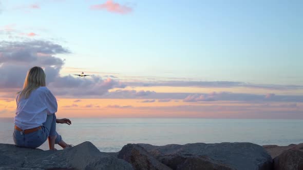 A woman sits on stones by the sea and looks at a beautiful sunset,