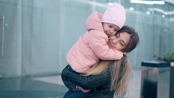 mother hugs a little daughter, they are in a business center