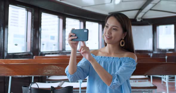 Woman use of smart phone to take photo on mobile phone and sit on star ferry in Hong Kong