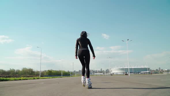 Athletic young woman riding the rollers in black tight leggings a flat asphalt road clear Sunny day