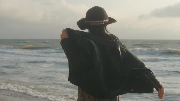 Portrait of Romantic Brunette Woman in Hat and Leather Jacket Walking on the Beach in Autumn at