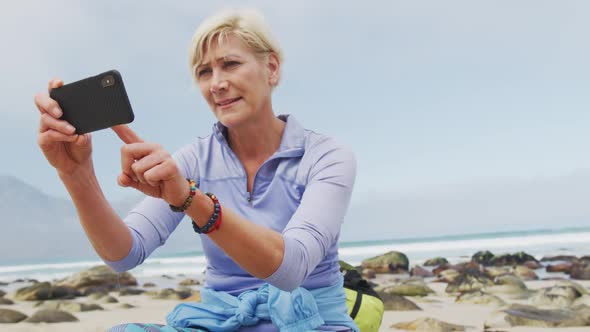 Senior hiker woman with backpack taking pictures using smartphone while sitting on rock